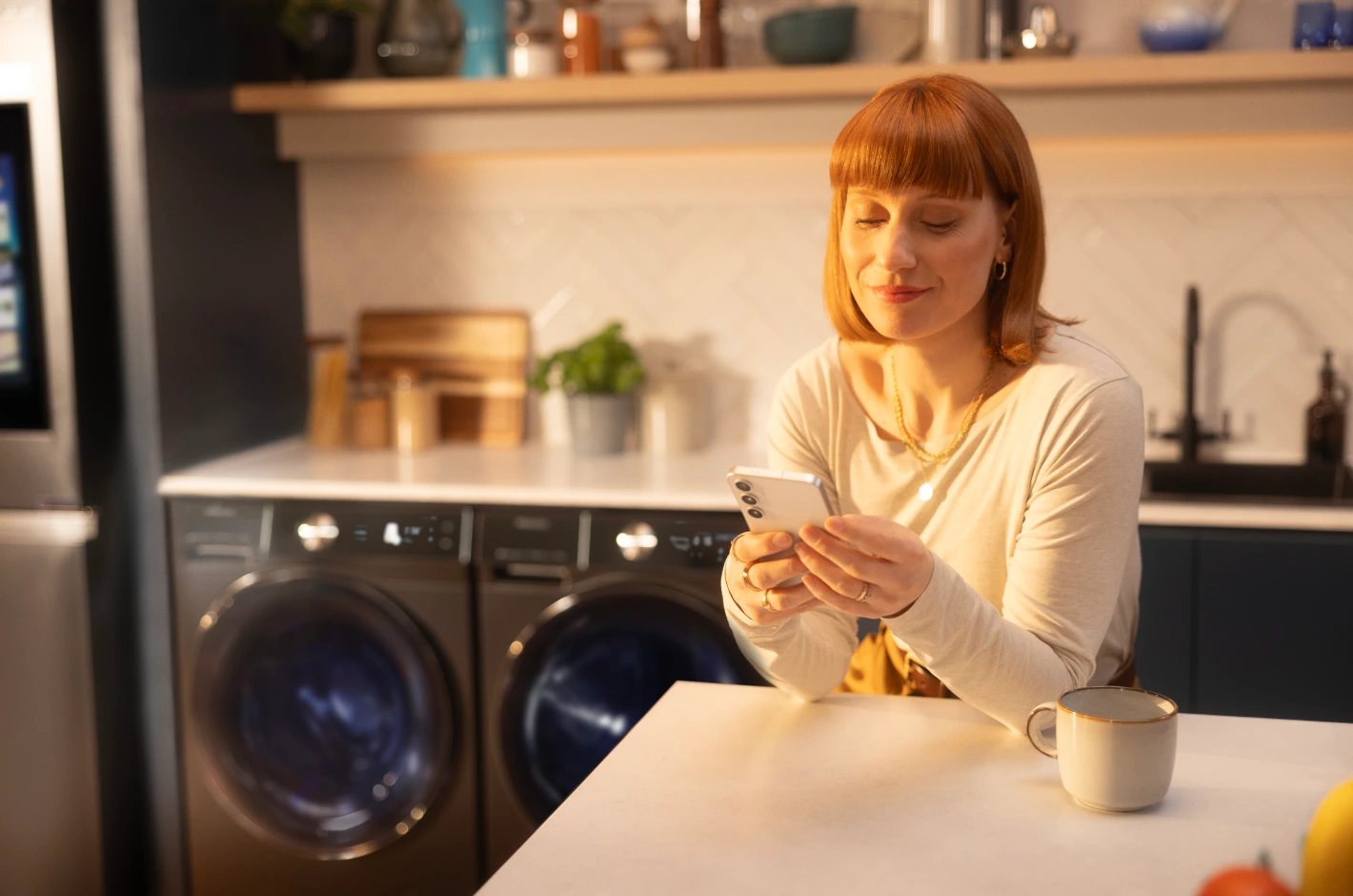 Lady at kitchen counter looking at mobile phone with Hisense smart kitchen products in background Lady at kitchen counter looking at mobile phone with Hisense smart kitchen products in background